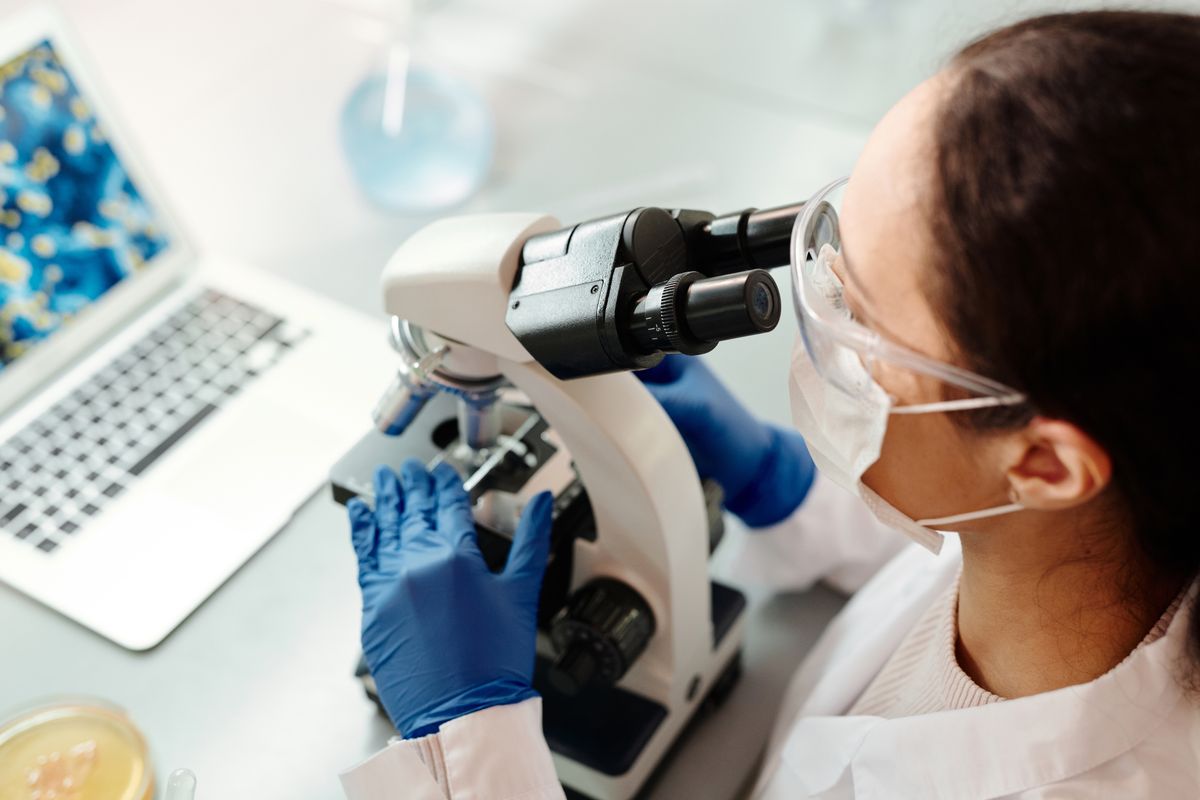 A researcher in protective gear examining samples with a microscope