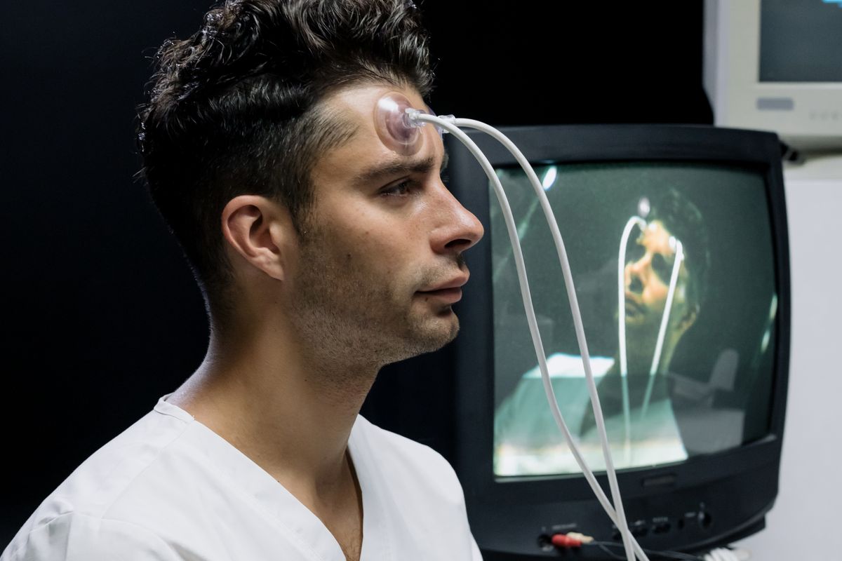 A man with a sensor attached to his forehead in a neurological monitoring room
