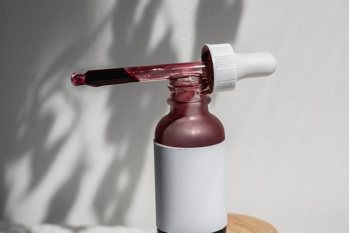 A serum bottle with a glass dropper on a plain background