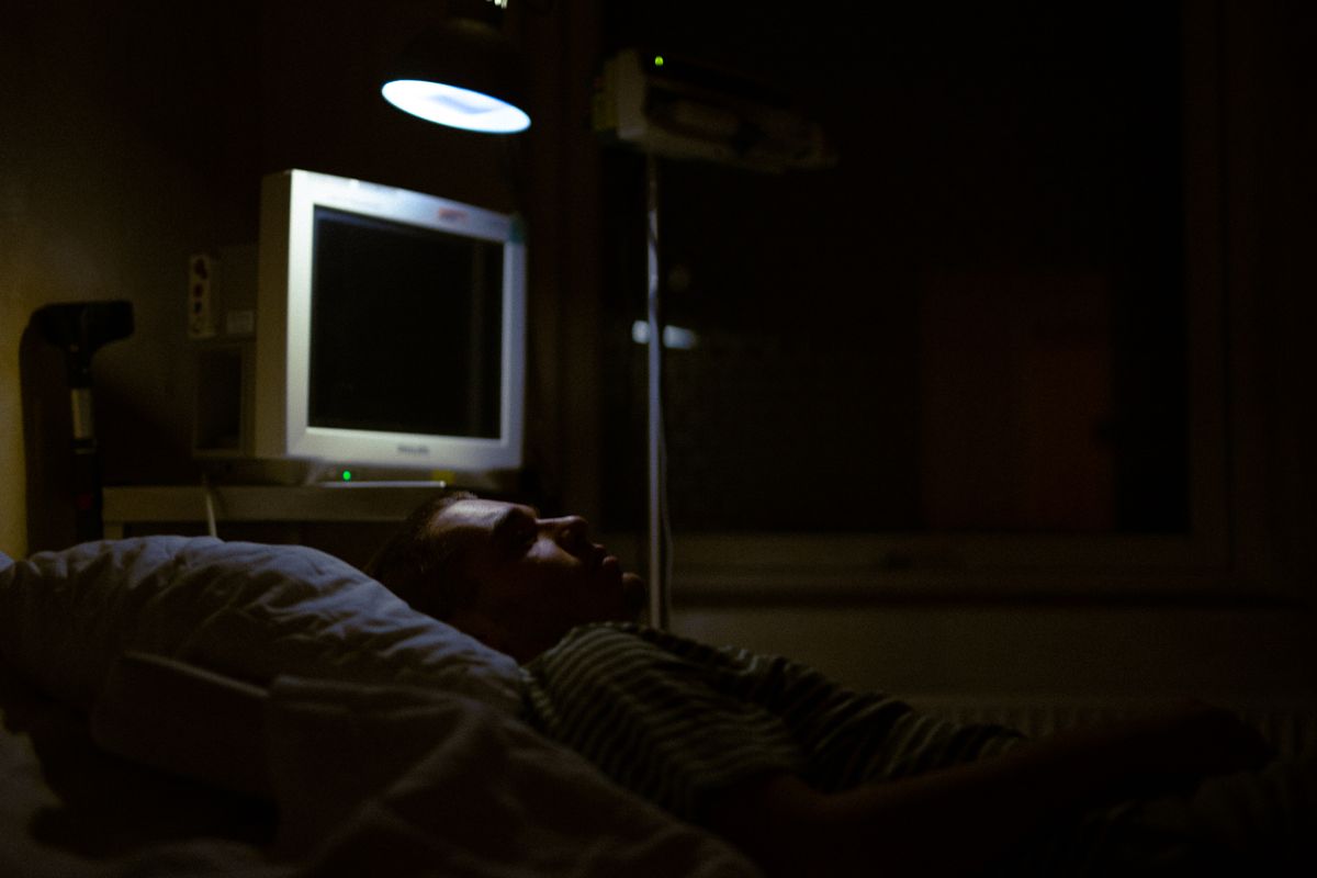 A person lying in a darkened clinical room beside a monitor