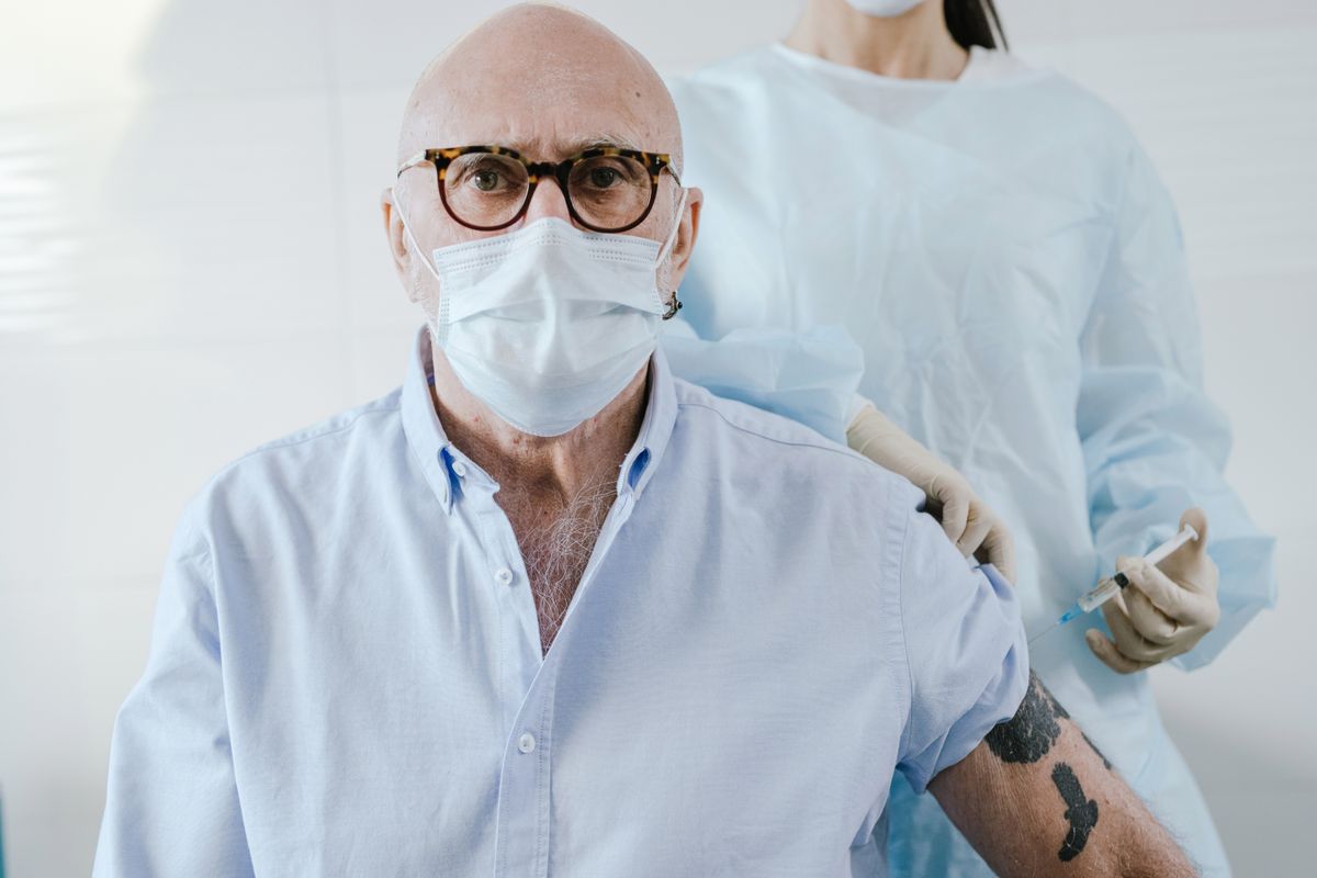 An older man receiving a vaccination from a clinician