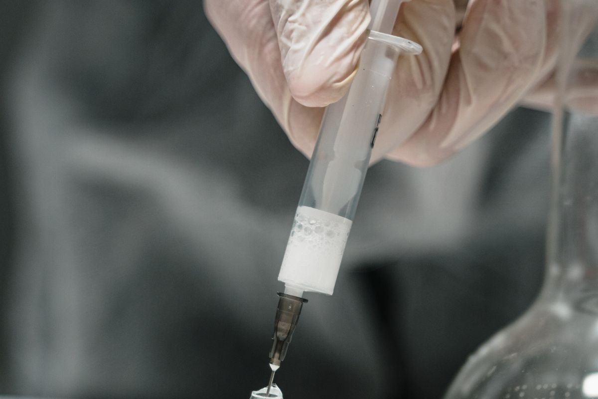 Gloved hands drawing liquid from a glass vial with a syringe